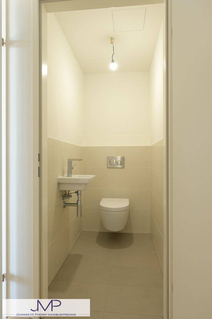 Gäste-WC mit wandhängender Toilette, kleinem Waschbecken und hellen Fliesen.