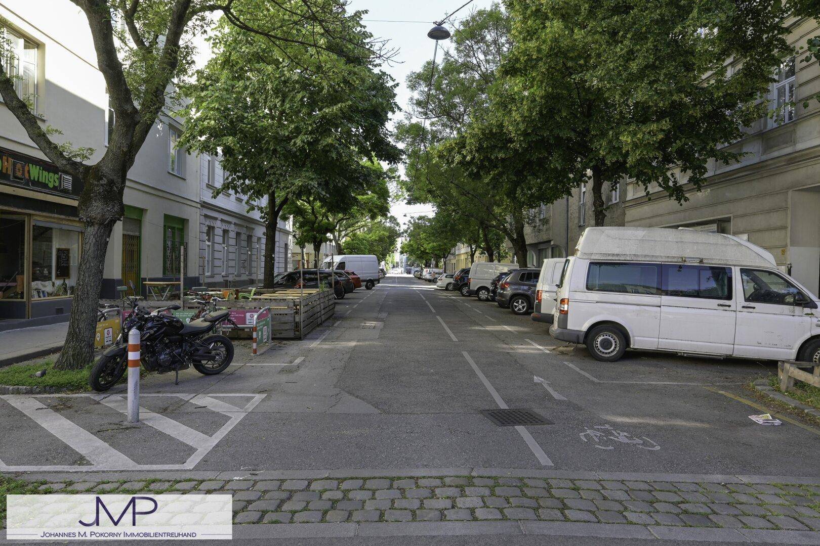 Ruhige Wohnstraße mit parkenden Autos und schattenspendenden Bäumen an einem sonnigen Tag.
