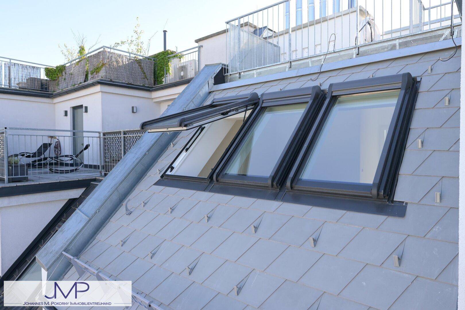 Dachfläche mit mehreren modernen Dachfenstern und Blick auf eine obere Terrasse.