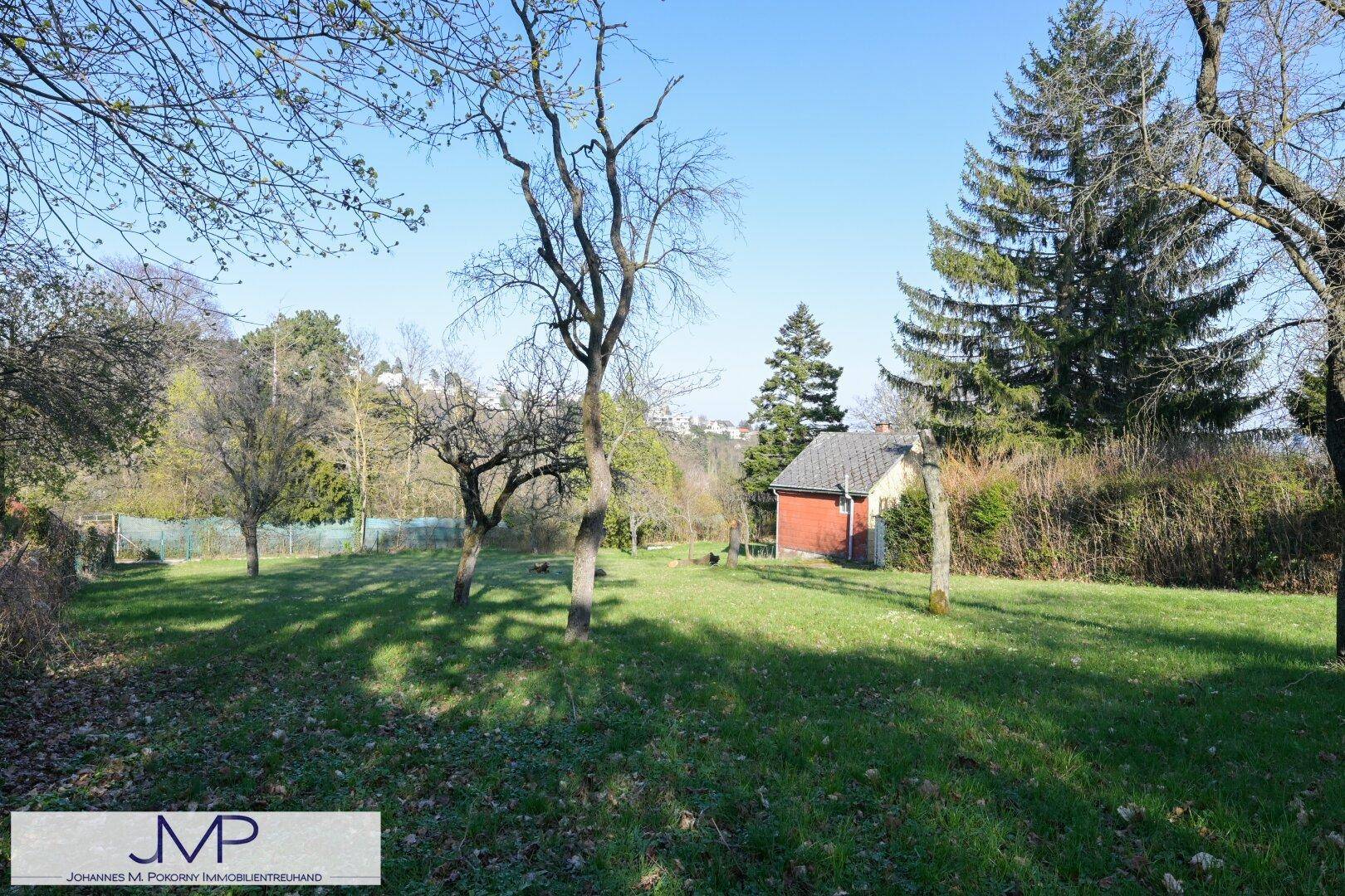 Großer Garten mit Rasen, alten Bäumen und einem kleinen roten Gartenhaus im Hintergrund.