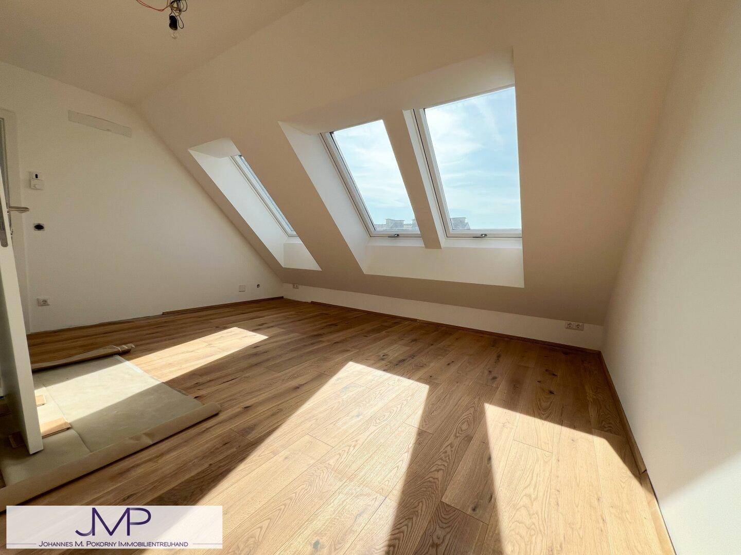Geräumiges Schlafzimmer mit Holzboden und drei Dachfenstern, bietet helle Wohnatmosphäre.