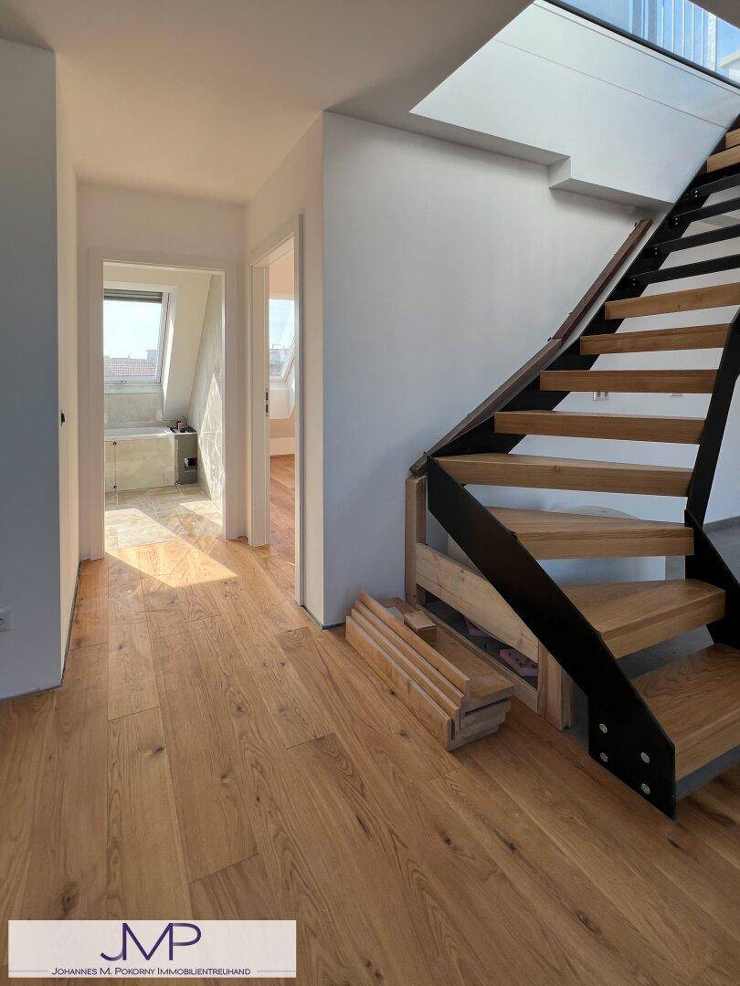 Heller Flurbereich mit Holzfußboden und moderner Treppe, führt zu weiteren Räumen.