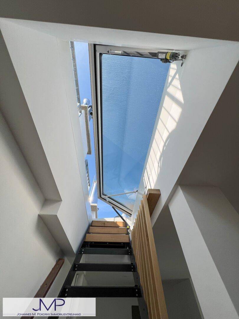 Moderne Treppe mit Holzstufen unter einem großen, lichtspendenden Dachfenster.