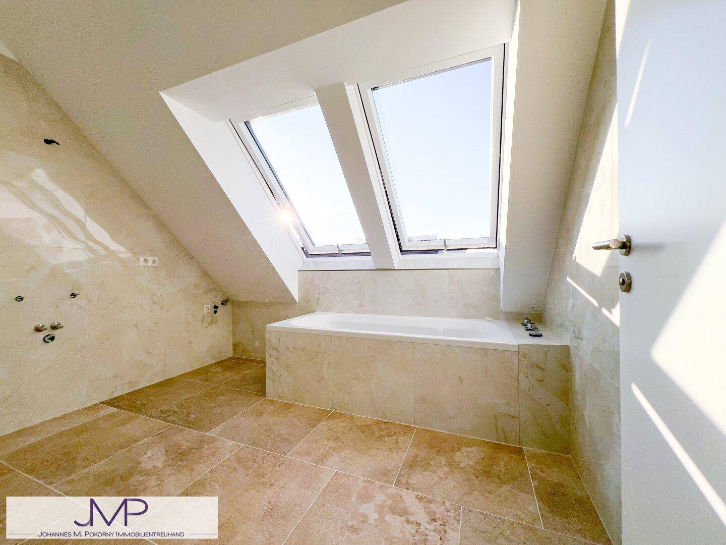Modernes Badezimmer im Dachgeschoss mit Badewanne, Fliesenboden und hellen Dachfenstern.