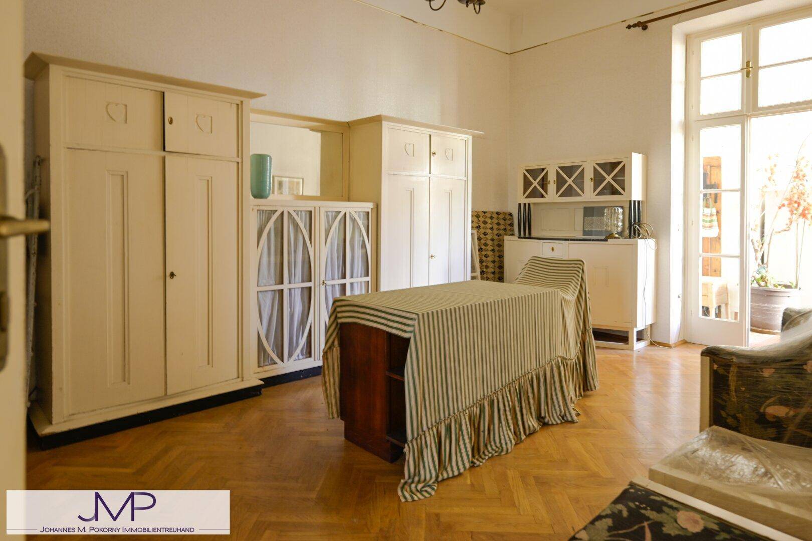 Geräumiges Schlafzimmer mit Parkettboden, großen Fenstern und Zugang zum Wintergarten.