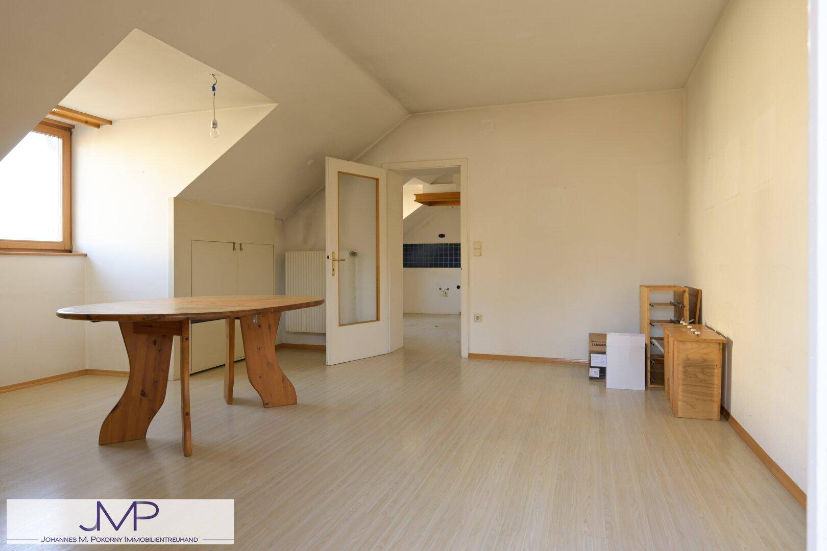 Helles Dachzimmer mit Schrägen, Laminatboden und Holztisch.