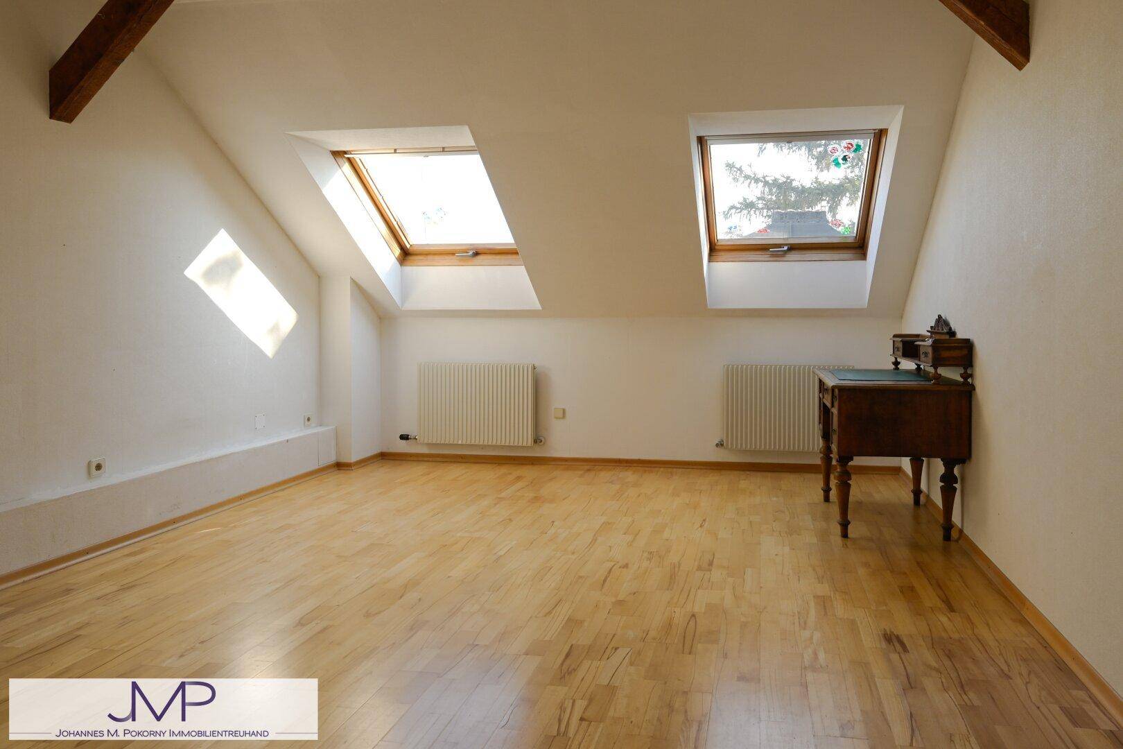 Geräumiges Dachzimmer mit Parkettboden und zwei Dachfenstern für viel Licht.