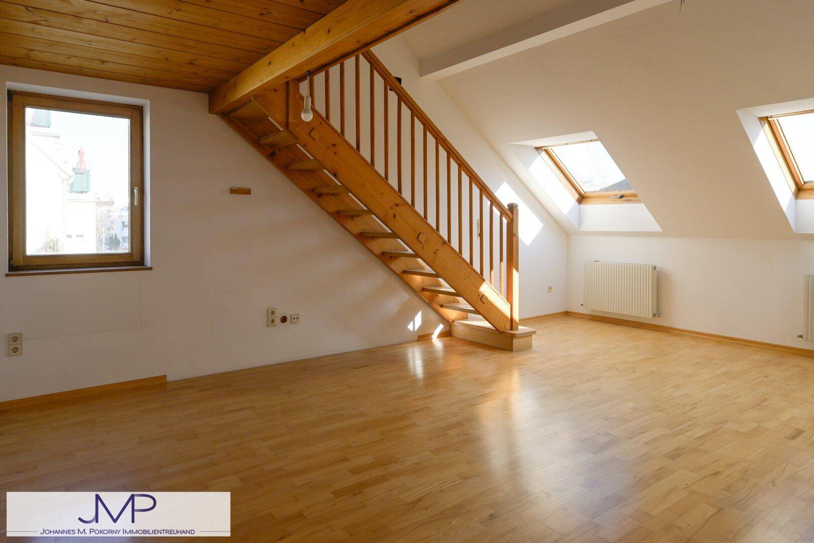 Geräumiges Dachzimmer mit Holztreppe, Parkettboden und Dachfenstern.