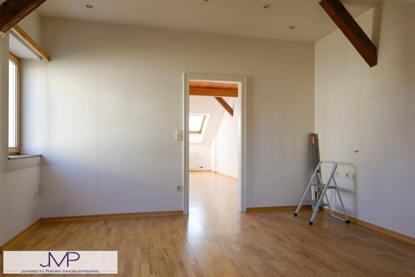 Helles Dachzimmer mit Parkettboden und Zugang zu einem weiteren Raum.