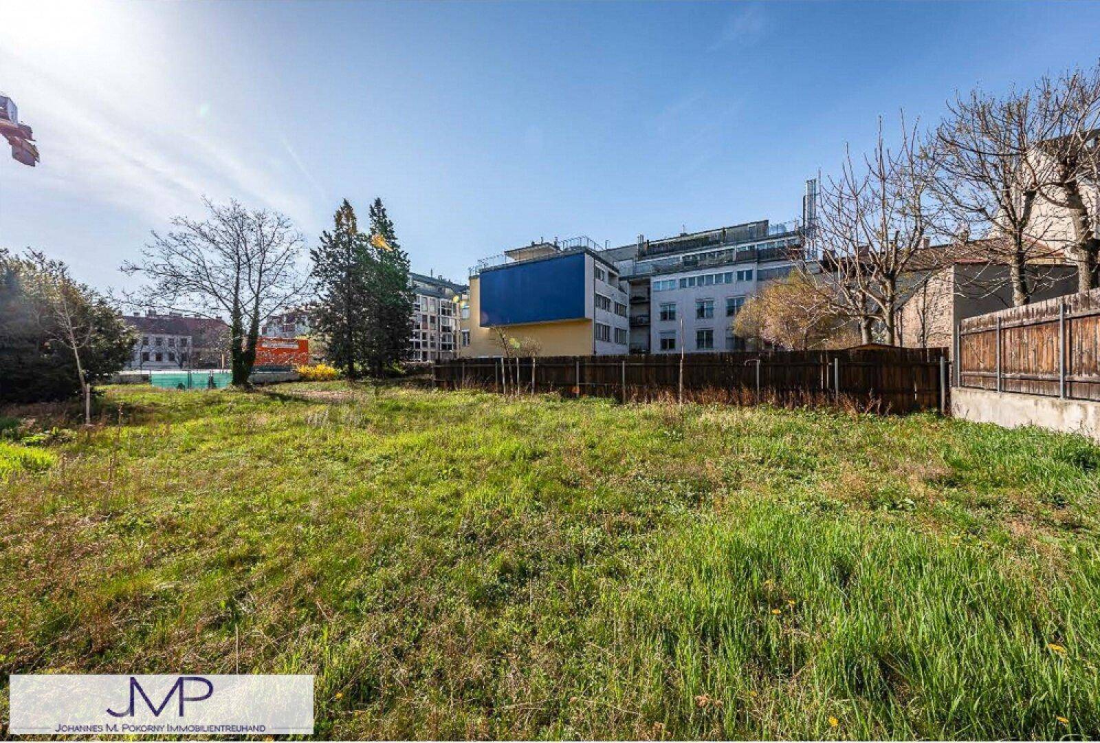 Sonniges Grundstück mit grüner Wiese und Blick auf moderne Gebäude in urbaner Umgebung.