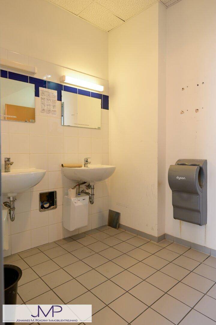 Waschraum mit zwei Waschbecken, Fliesenboden und einem modernen Händetrockner an der Wand.