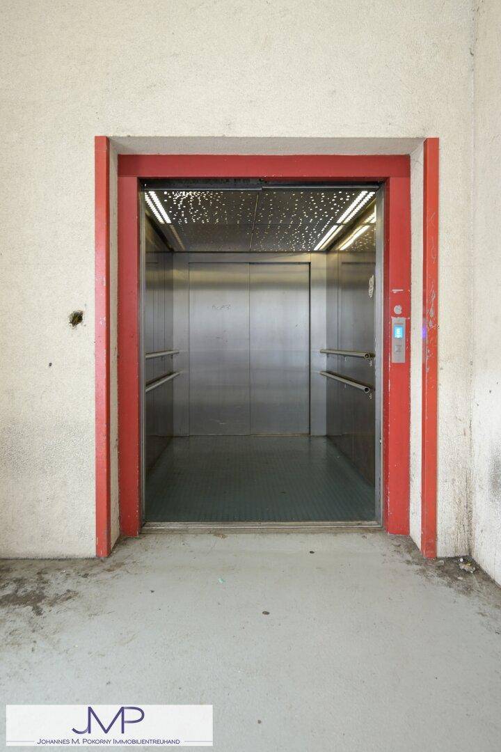 Offener Aufzug mit Edelstahlinnenraum und rotem Rahmen, bereit zur Benutzung.