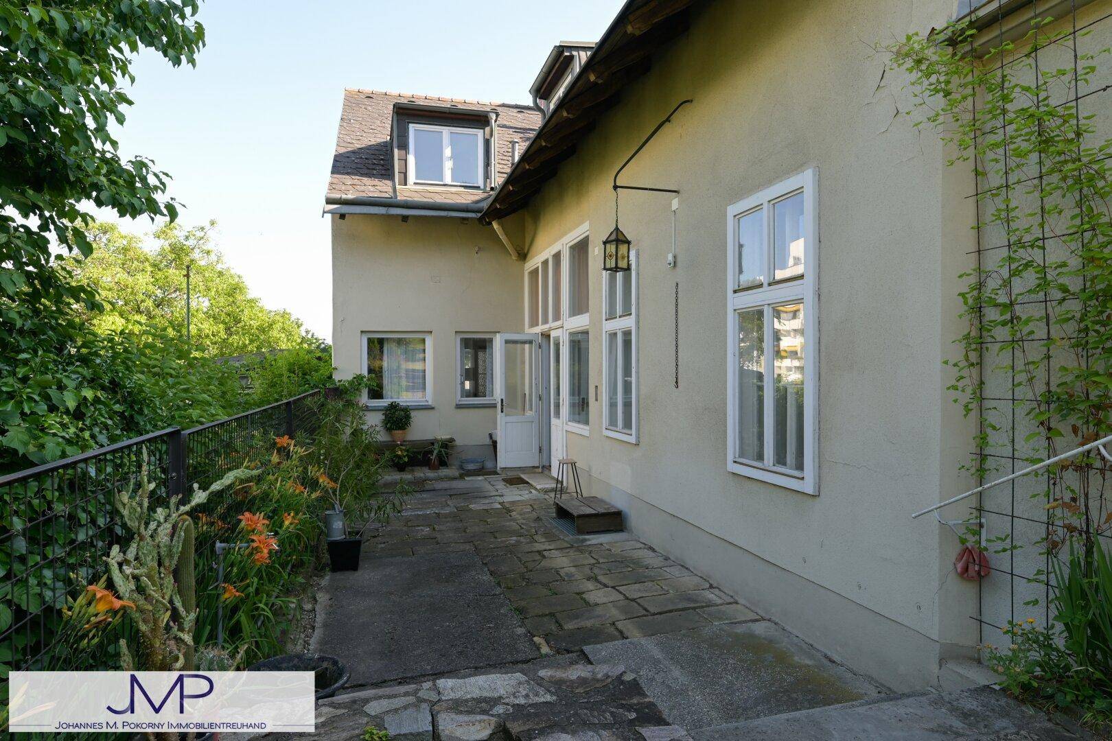 Seitliche Terrasse mit Steinplatten, umgeben von Pflanzen und mit Zugang zum Haus.