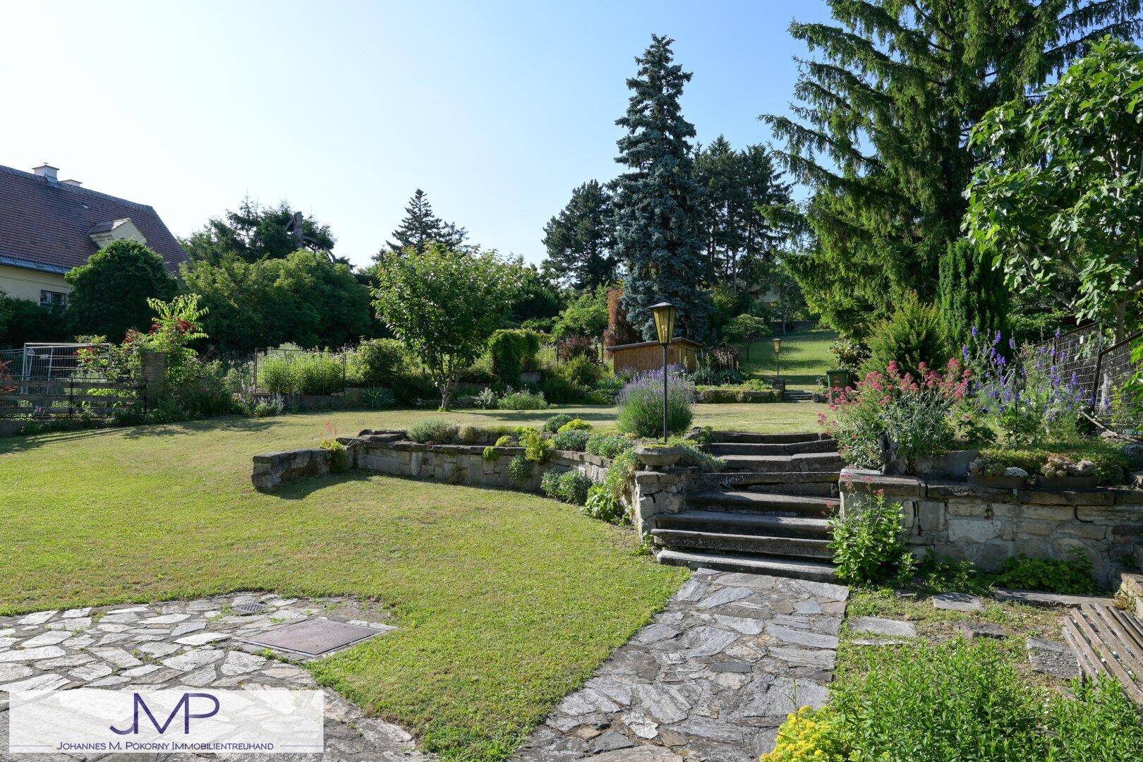 Großer Garten mit Rasenflächen, Steinmauern und Treppen, die zu verschiedenen Ebenen führen.