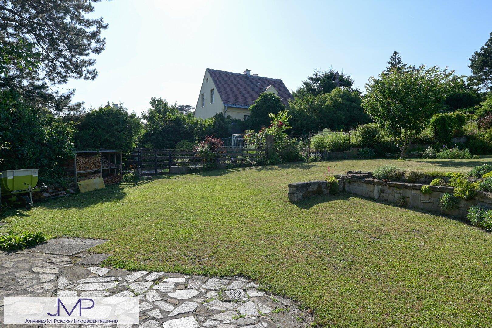 Weitläufiger Garten mit Rasenfläche und einem Haus im Hintergrund, umgeben von Bäumen.