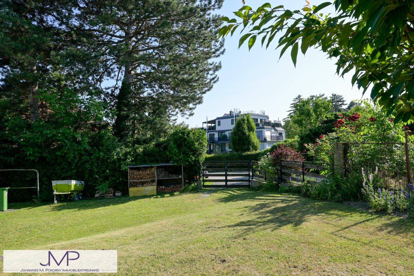 Großer Gartenbereich mit Rasen, Holzlager und einem Zaun, der das Grundstück begrenzt.