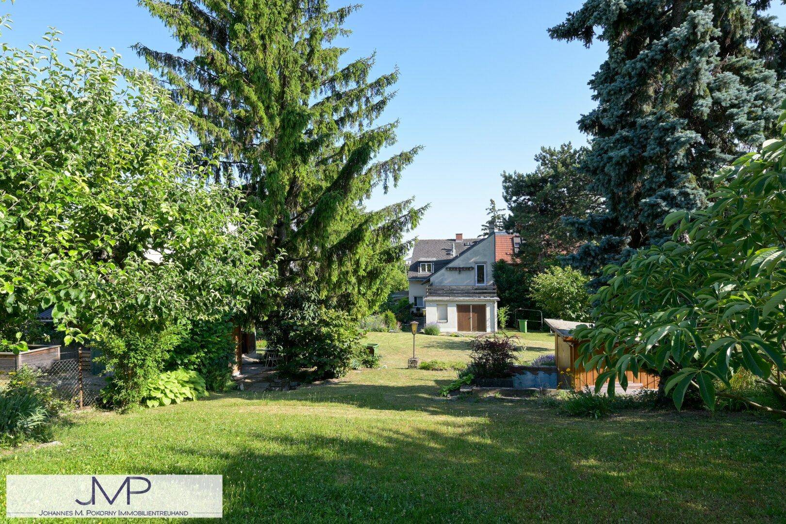 Weitläufiger Garten mit Rasenflächen und Bäumen, im Hintergrund ist ein weiteres Gebäude sichtbar.