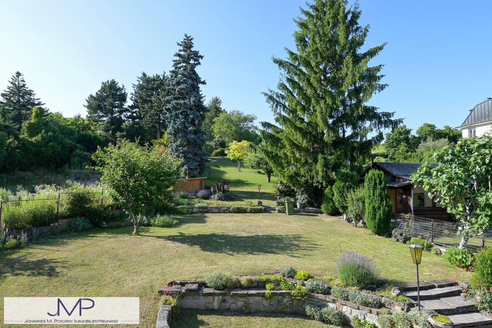 Weitläufiger, gepflegter Garten mit Rasenflächen, Blumenbeeten und altem Baumbestand.