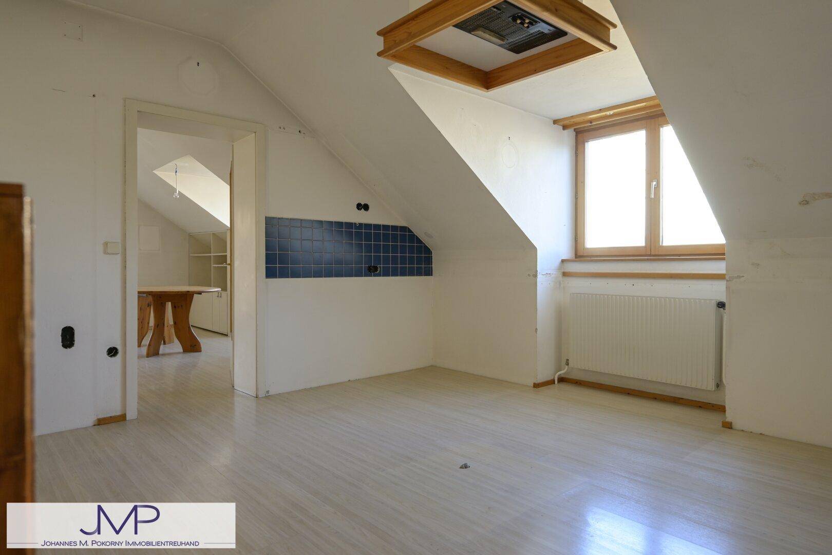 Dachgeschossraum mit schrägen Wänden, Laminatboden und einem Fenster, das Tageslicht hereinlässt.