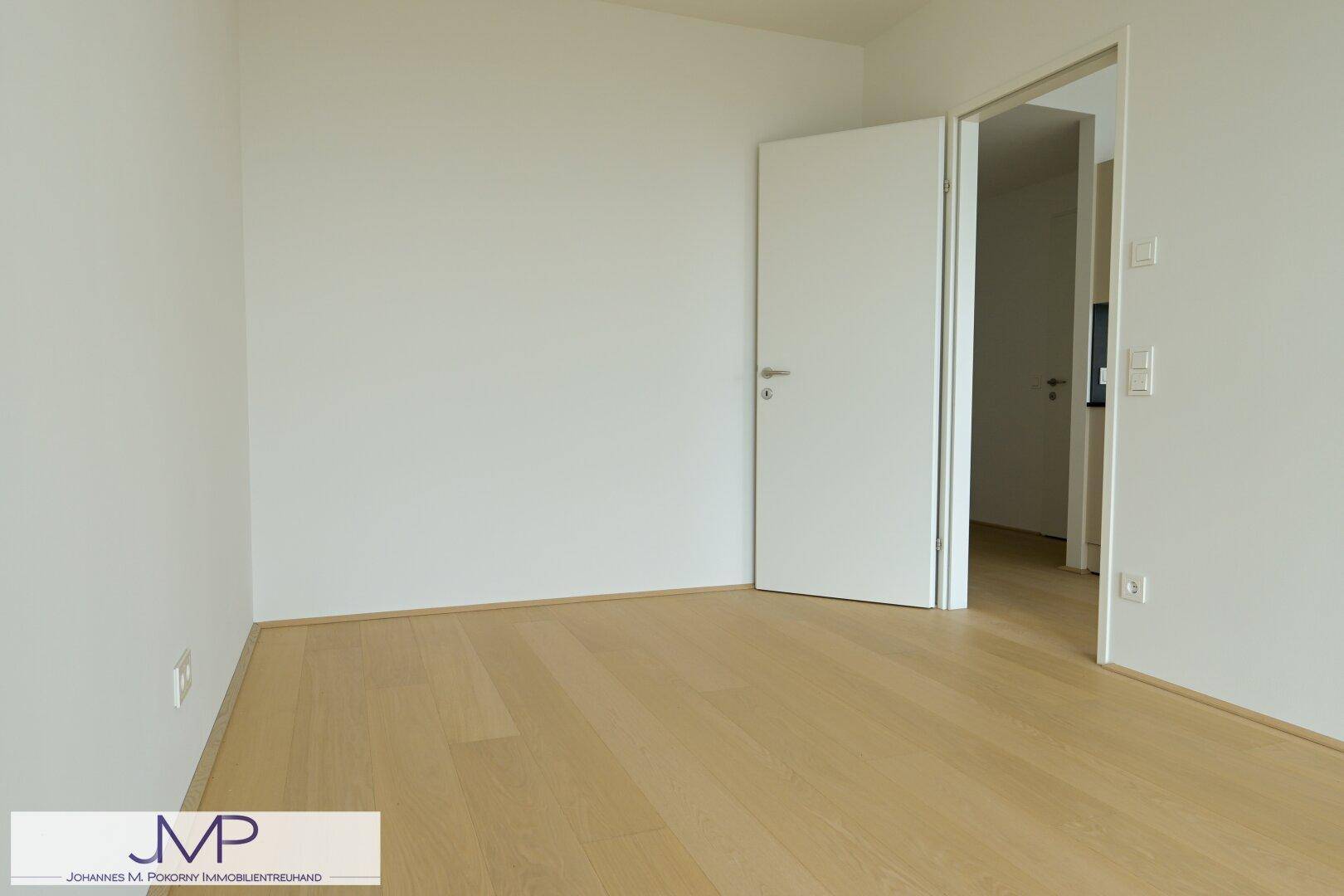 Helles, leeres Zimmer mit Holzboden und weiß gestrichenen Wänden, bereit zum Einzug.