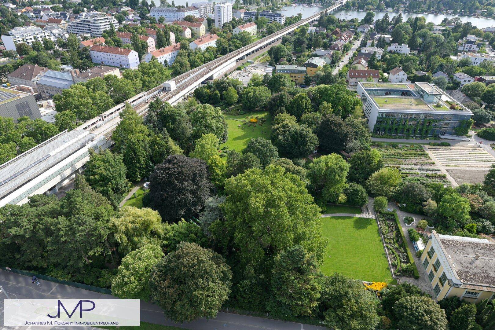 Luftaufnahme eines weitläufigen Parks mit üppigem Grün und einer erhöhten Bahntrasse.