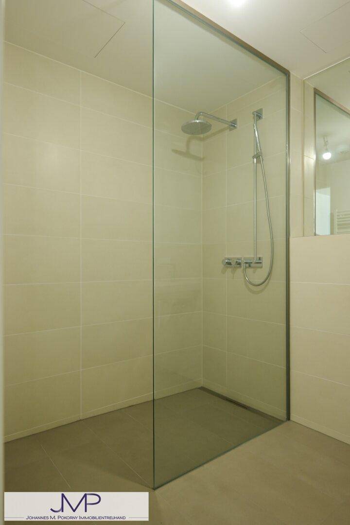 Geräumige, begehbare Dusche mit Glaswand und Regenduschkopf in modernem Badezimmer.