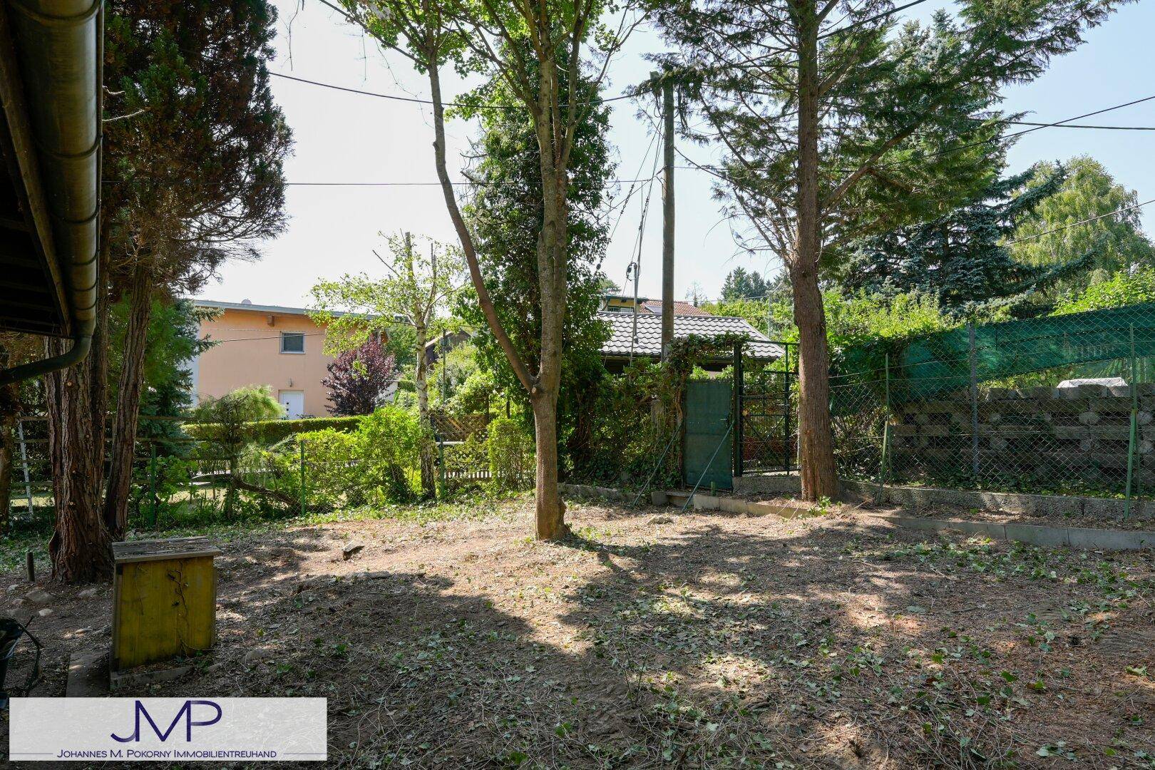 Weitläufiger Gartenbereich mit Bäumen und einem kleinen Gartenhaus im Hintergrund, umgeben von Natur.