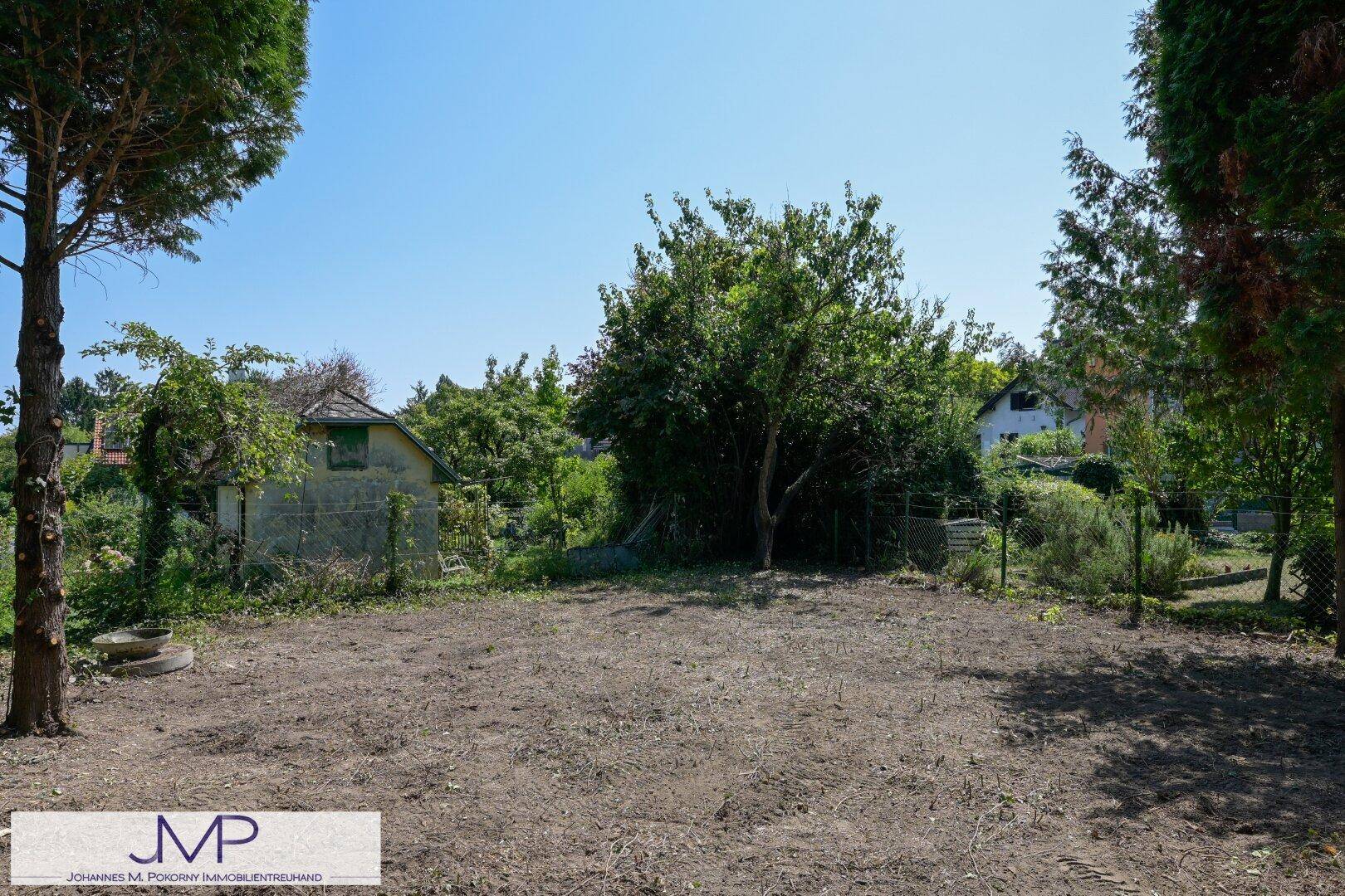 Große Gartenfläche mit verschiedenen Bäumen und einem älteren Gebäude im Hintergrund.