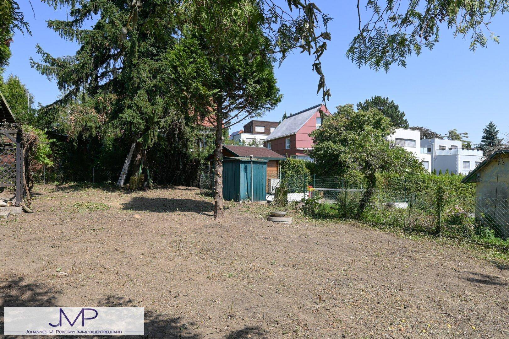 Gartenbereich mit einem kleinen Schuppen und umliegenden Wohnhäusern im Hintergrund.