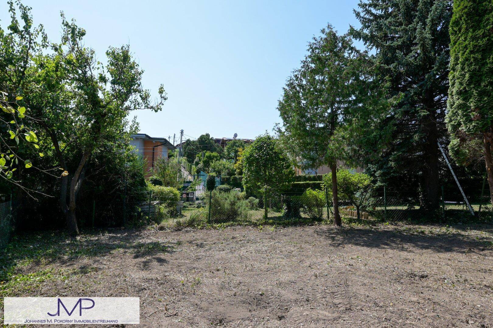 Offener Gartenbereich mit Bäumen und Blick auf weitere Gärten und Häuser in der Ferne.