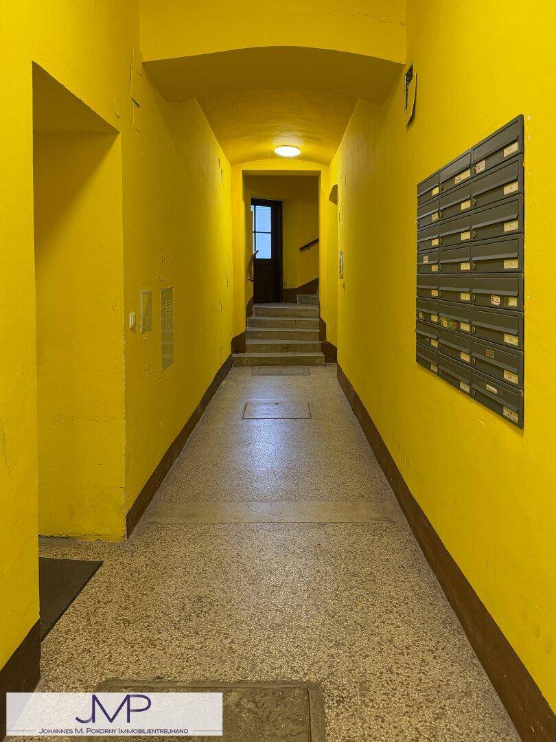 Langer, gelb gestrichener Flur mit Terrazzoboden und Briefkästen an der Wand.