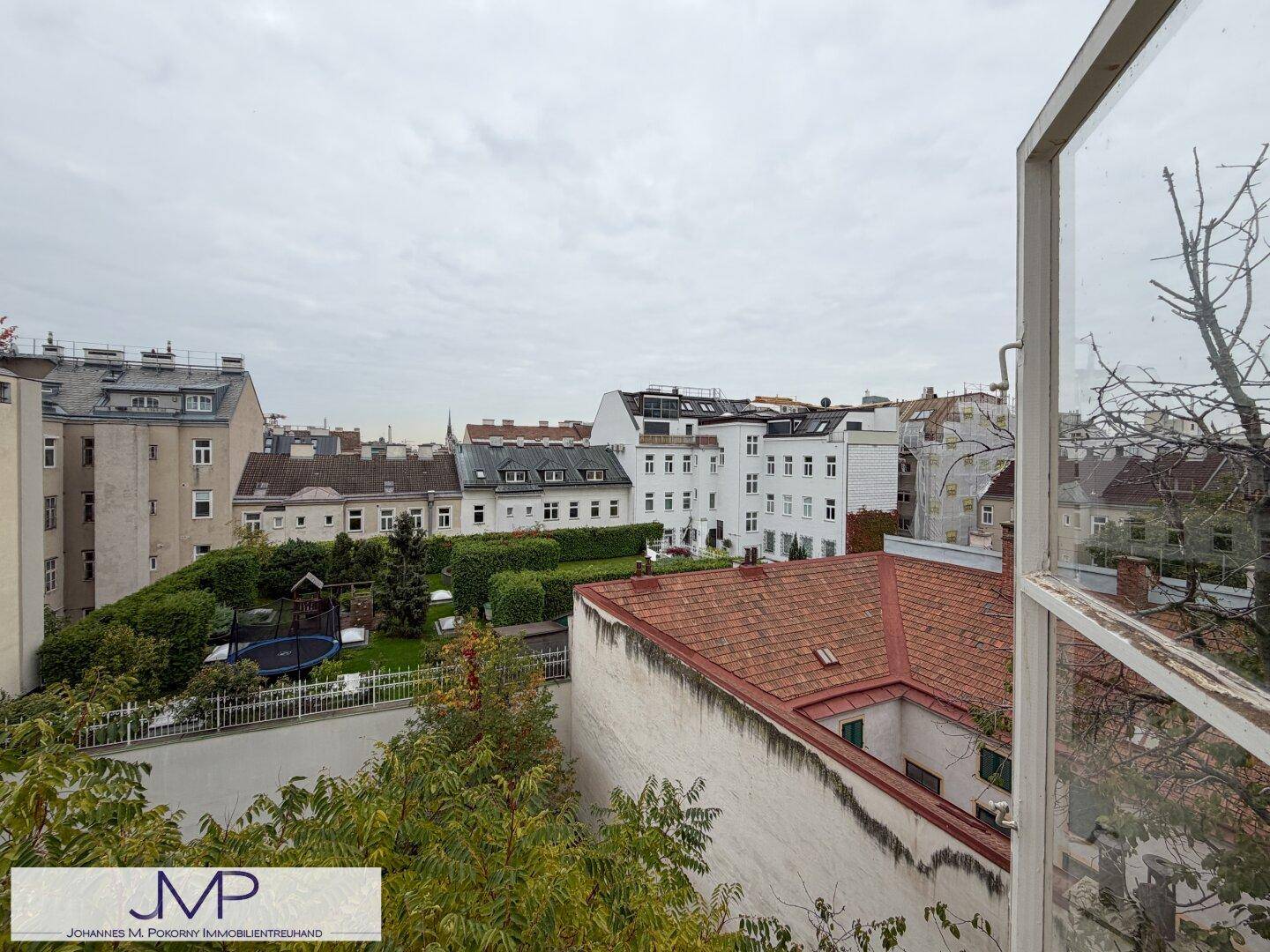 Weitläufiger Stadtblick über Dächer und Gärten von einem oberen Stockwerk.