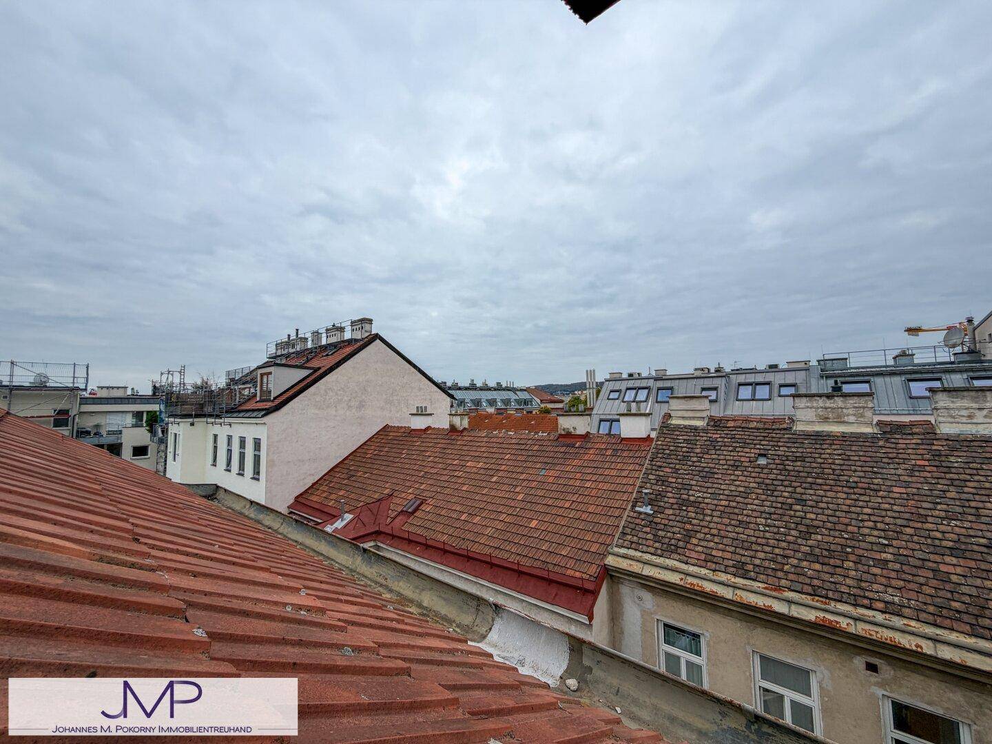 Blick über die roten Ziegeldächer der umliegenden Gebäude unter bewölktem Himmel.