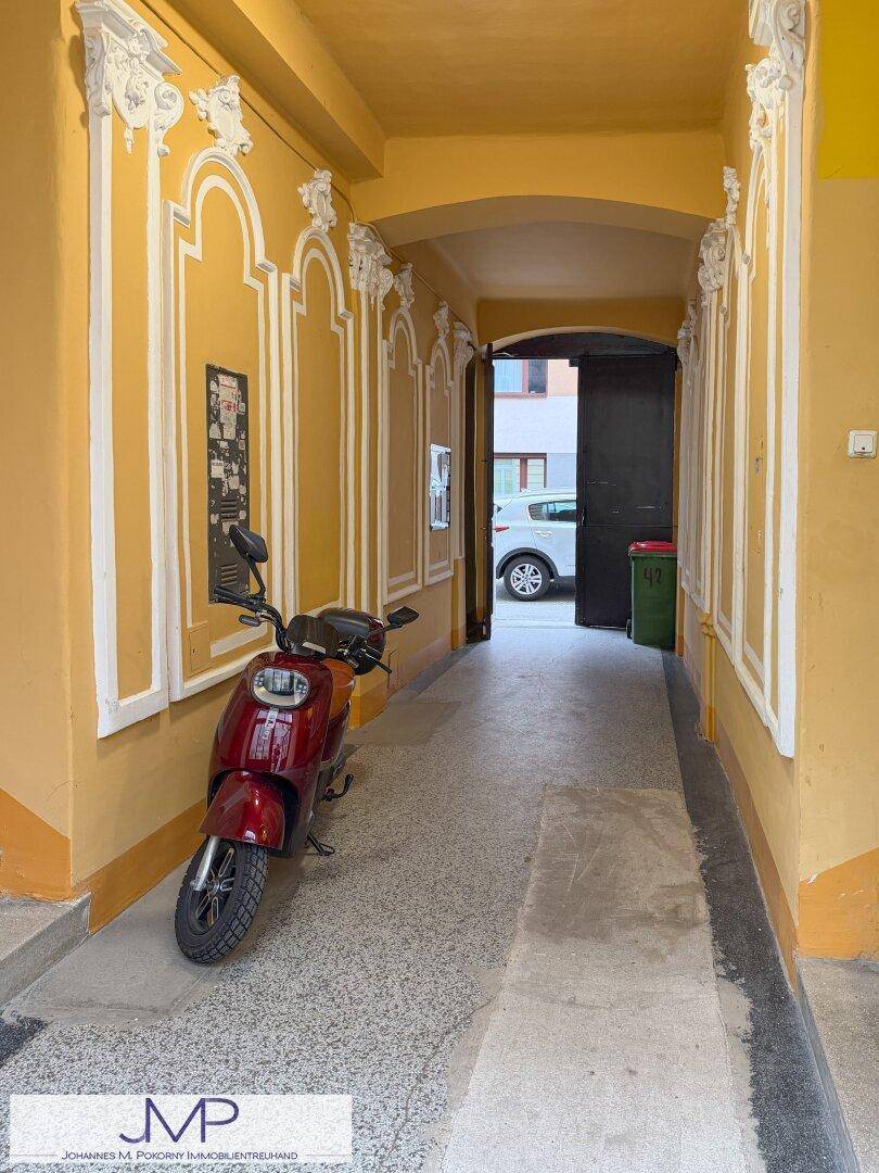 Heller Eingangsbereich mit Terrazzoboden, dekorativen Stuckelementen und einem Roller.