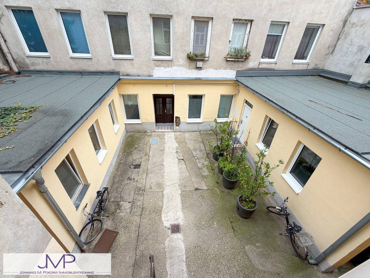 Vogelperspektive auf den gepflasterten Innenhof, umgeben von Gebäuden und einigen Pflanzen.