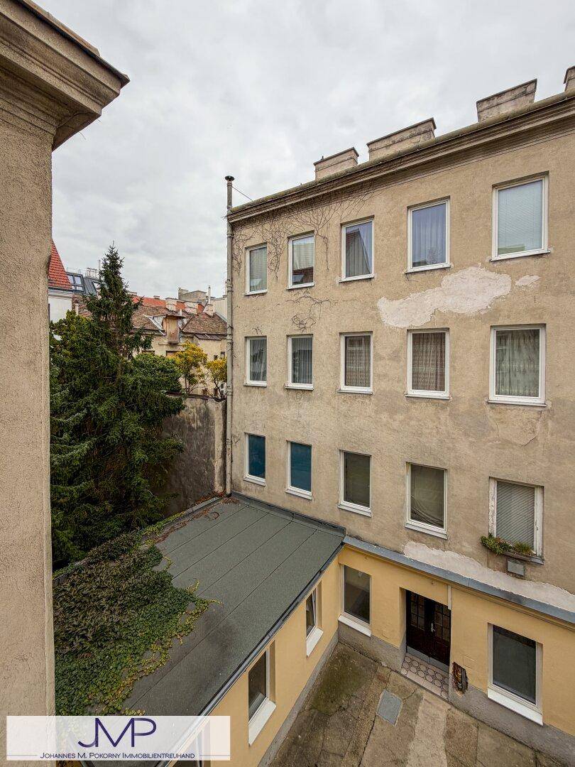Blick auf den Innenhof und die Rückseite eines Gebäudes mit vielen Fenstern und Bäumen.