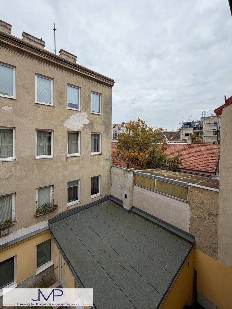 Blick über einen Innenhof auf die Dächer benachbarter Gebäude unter bewölktem Himmel.