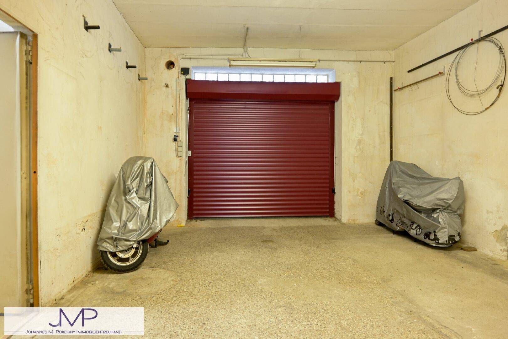 Garage mit rotem Rolltor und Platz für Fahrzeuge, inklusive Motorrädern.
