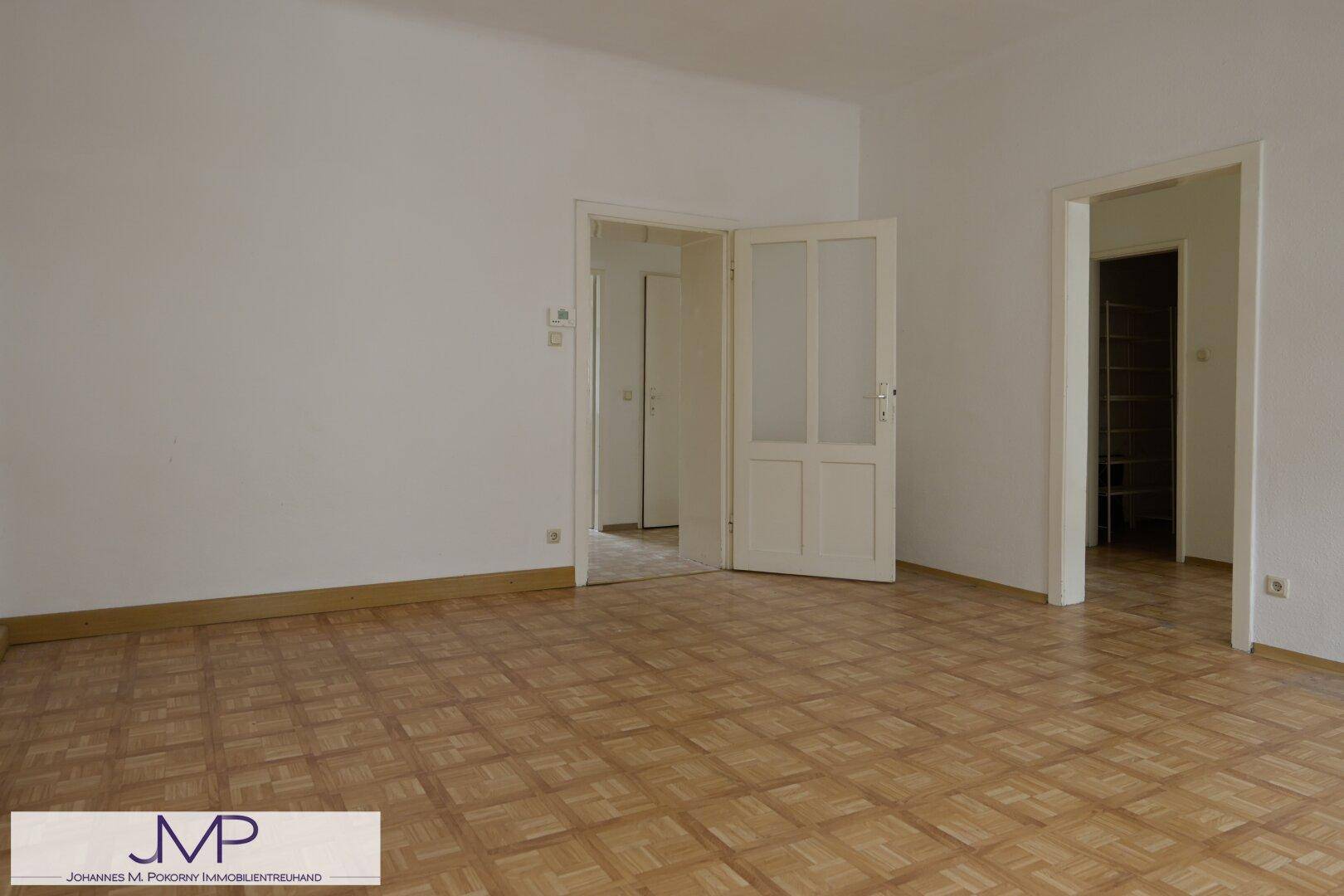 Helles Wohnzimmer mit Parkettboden und mehreren Türen zu angrenzenden Räumen.