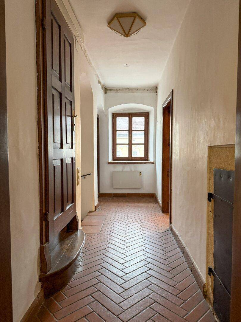 Langer Flur mit Terrakotta-Fischgrätboden, weiß gestrichenen Wänden und einem Fenster am Ende.