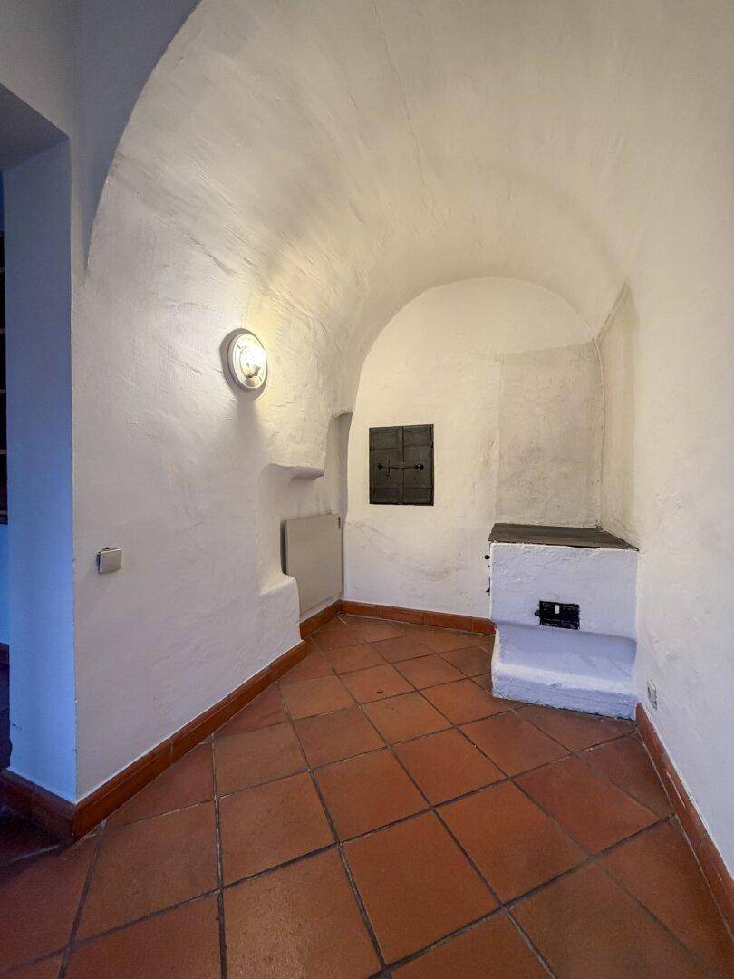 Gewölbter Flur mit Terrakottafliesen und einem traditionellen Kachelofen, der eine gemütliche Atmosphäre schafft.