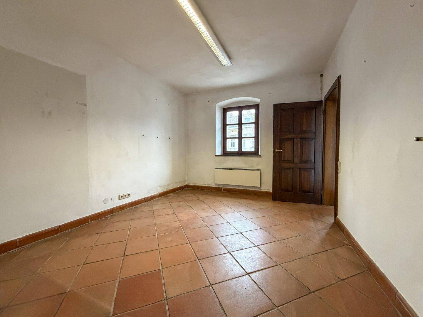 Leerer Raum mit Terrakottafliesen, einem einzelnen Fenster und einer einfachen Deckenleuchte.