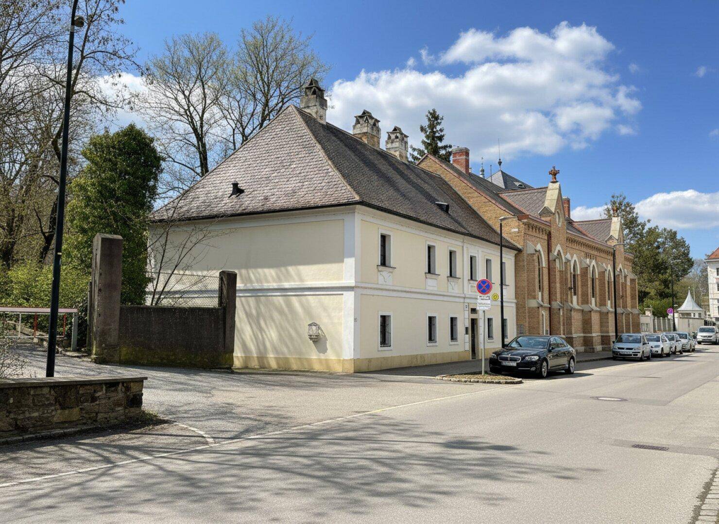 Historisches Gebäude von der Straßenseite aus gesehen, mit beiger Fassade und einem angrenzenden Backsteingebäude.
