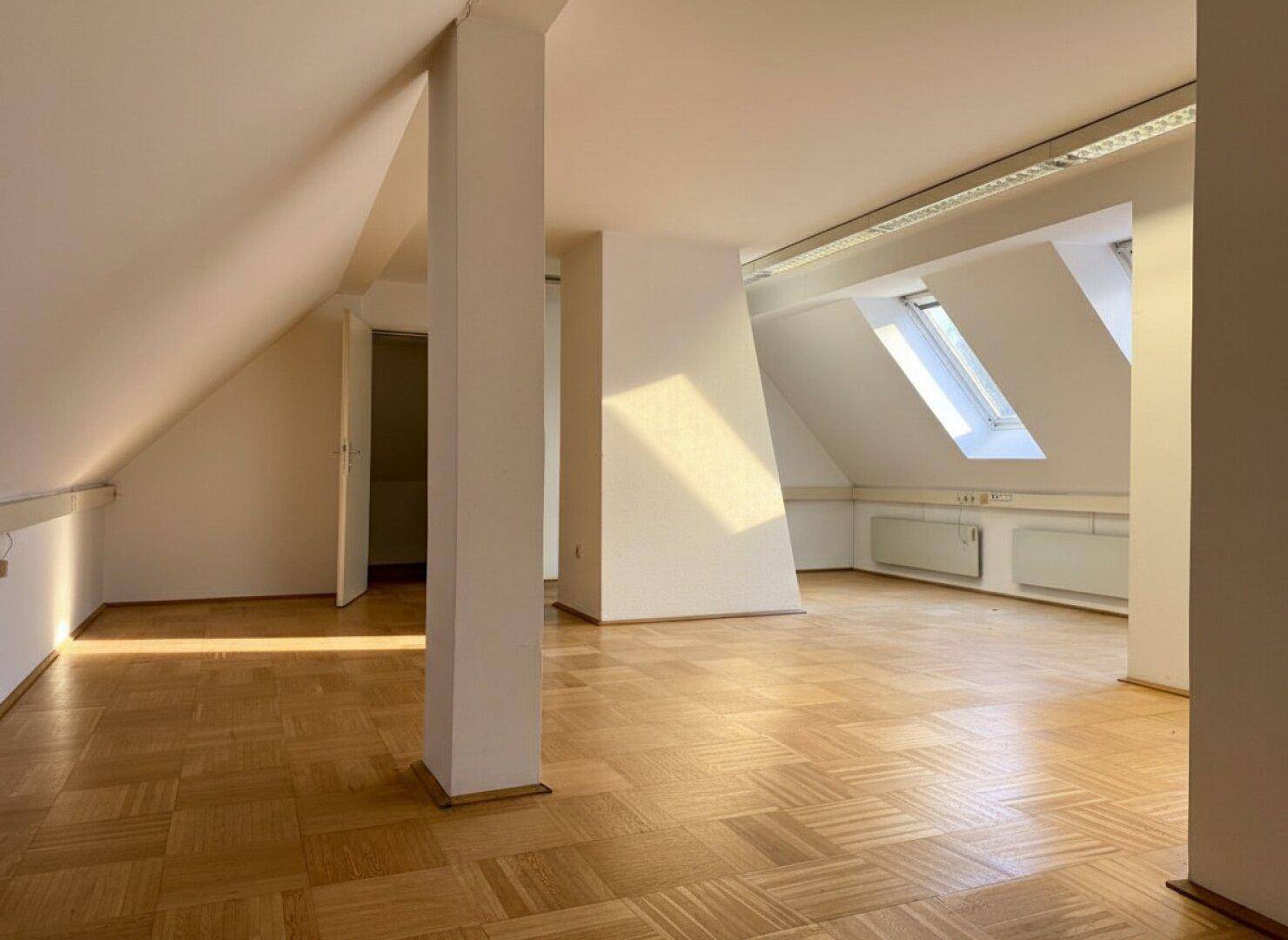 Heller Dachbodenraum mit Parkettboden, schrägen Wänden und mehreren Dachfenstern, die viel Licht hereinlassen.