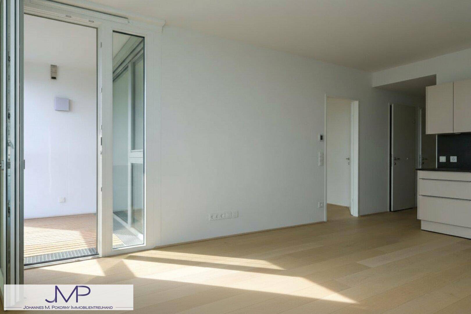 Heller Wohnbereich mit Holzboden und großem Fenster, das Zugang zum Balkon bietet.
