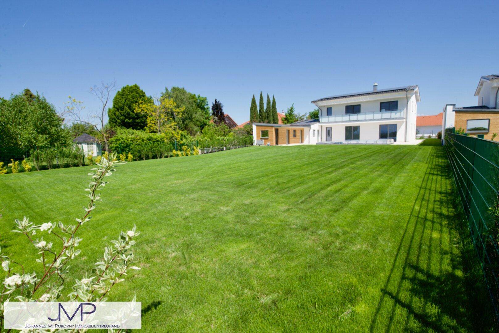 Großer, gepflegter Garten mit weitläufigem Rasen und modernem Haus im Hintergrund.