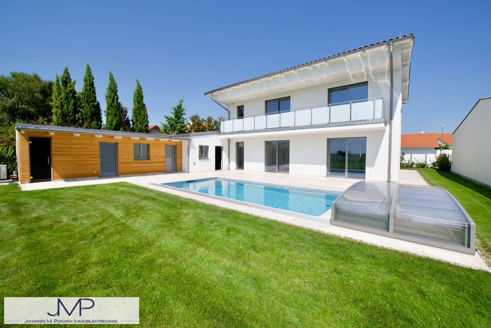 Modernes Haus mit großem Garten, offenem Pool und Holz-Nebengebäude unter blauem Himmel.