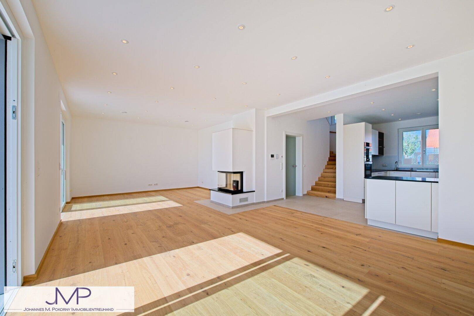 Helles, offenes Wohnzimmer mit Eichenparkett, modernem Kamin und Zugang zur Küche.