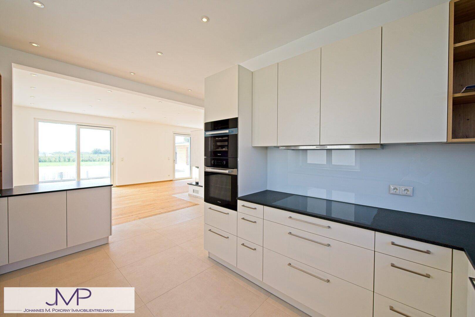 Moderne Einbauküche mit weißen Schränken, dunklen Arbeitsplatten und Blick ins Wohnzimmer.