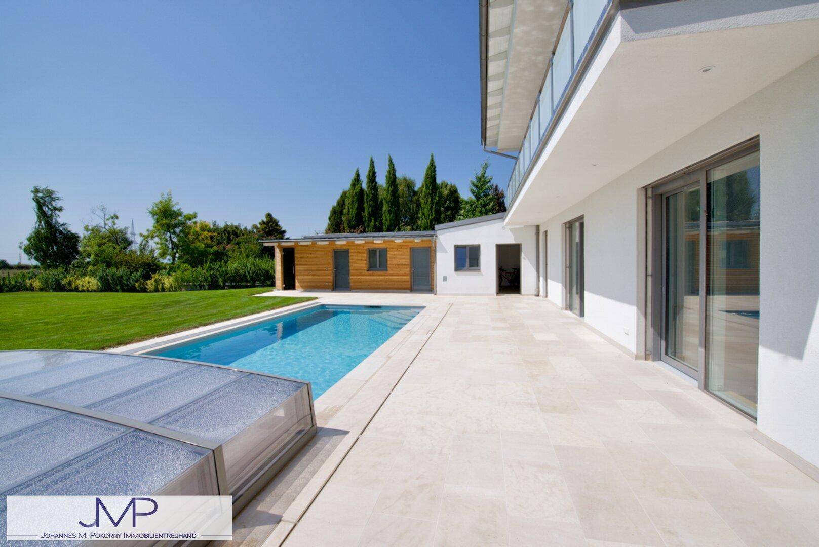 Geräumige Terrasse am Haus mit Blick auf den Pool und das Holz-Nebengebäude.